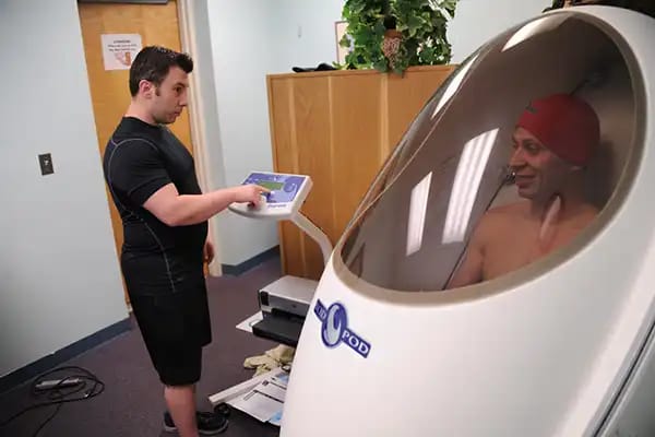 A man undergoing a precise body composition test inside an Air Displacement Plethysmography (Bod Pod) chamber.