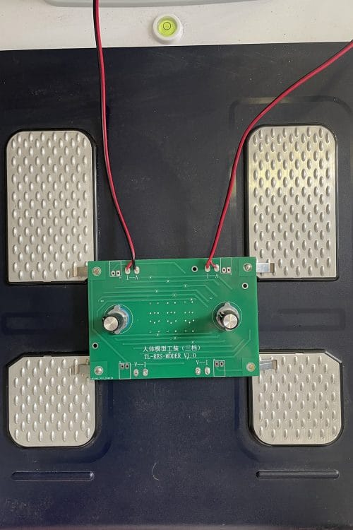 The iBodyinfo RES-MODER human impedance simulator placed on the footplate electrodes of a smart scale for production line quality control.