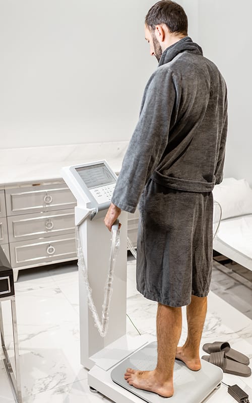 A man stands barefoot on a professional stand-on body composition analyzer for a complete body composition test in a clinical setting.